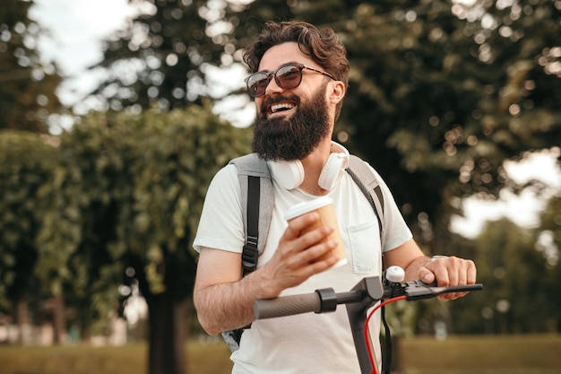 Heureux hipster avec boisson équitation scooter