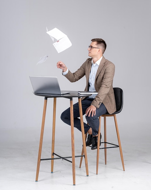 Heureux homme d'affaires assis au bureau et jetant des documents en l'air. Célébrer une heureuse nouvelle.