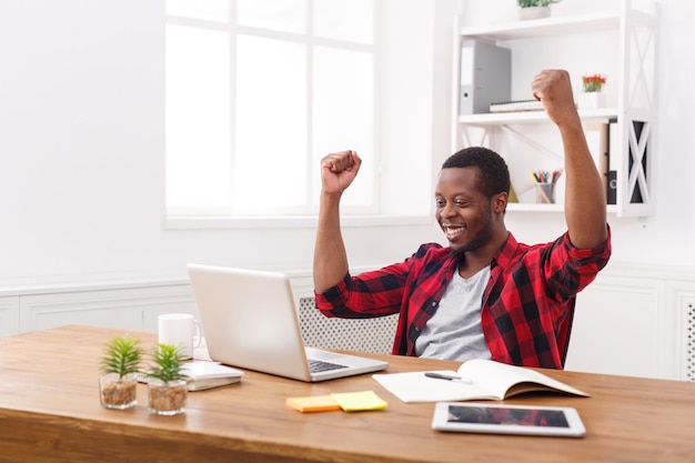 Heureux homme d'affaires célébrer, gagner. Gagnant, homme noir au bureau avec ordinateur portable