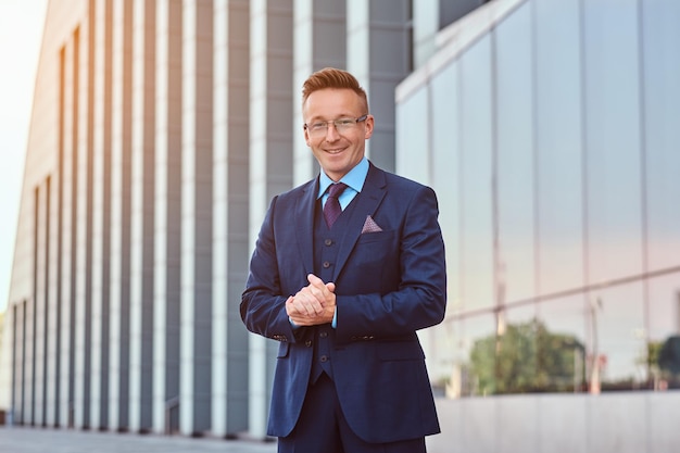 Heureux homme d'affaires confiant vêtu d'un costume élégant debout à l'extérieur sur un fond de paysage urbain.