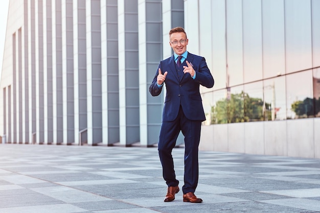 Heureux homme d'affaires confiant vêtu d'un costume élégant debout à l'extérieur sur un fond de paysage urbain.