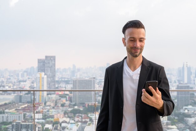 Heureux homme d'affaires debout sur le toit d'un gratte-ciel à l'aide de téléphone mobile