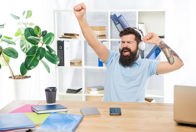 Heureux homme d'affaires faisant un geste gagnant en écoutant des écouteurs dans la musique de bureau