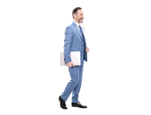 Heureux homme d'affaires grisonnant en costume pleine longueur marchant avec ordinateur isolé sur blanc business