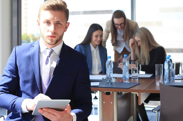 Heureux homme d'affaires intelligent avec des coéquipiers discutant en arrière-plan