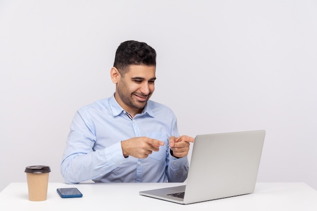 Heureux homme d'affaires joyeux assis au travail de bureau pointant du doigt l'écran d'un ordinateur portable parlant par appel vidéo ayant une communication en ligne avec un collègue studio intérieur tourné isolé sur fond blanc