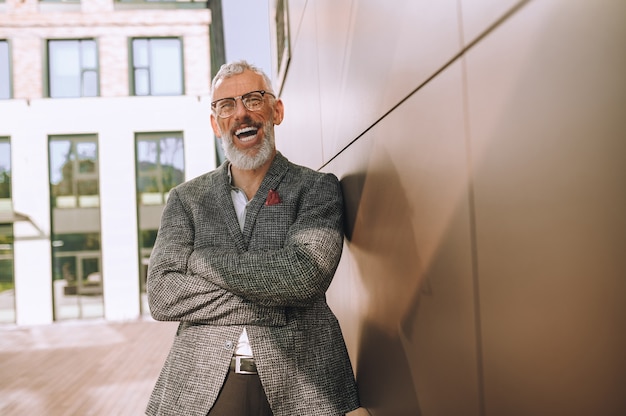 Heureux homme d'affaires à lunettes mature debout près du mur