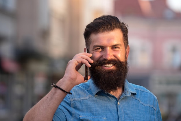 Heureux homme d'affaires moderne hipster avec barbe marchant en ville et appelant sur téléphone mobile.