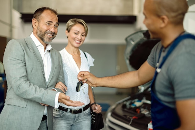 Heureux homme d'affaires recevant des clés de voiture d'un mécanicien dans un atelier de réparation automobile