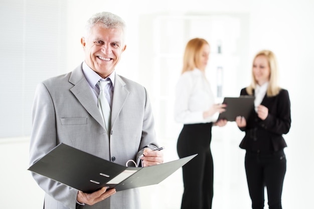 Heureux homme d'affaires senior avec dossier debout au bureau. Regarder la caméra. Mise au point sélective.