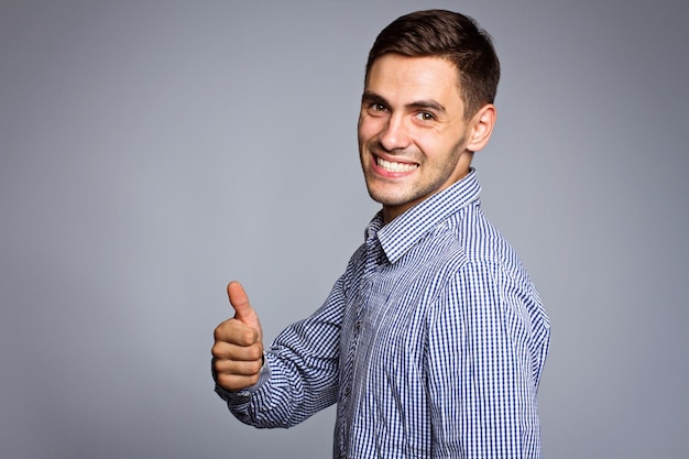 Heureux homme d'affaires souriant avec le geste du pouce levé sur fond gris