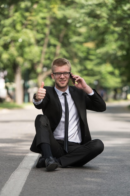 Heureux homme d'affaires utilisant un téléphone portable à l'extérieur assis sur l'asphalte