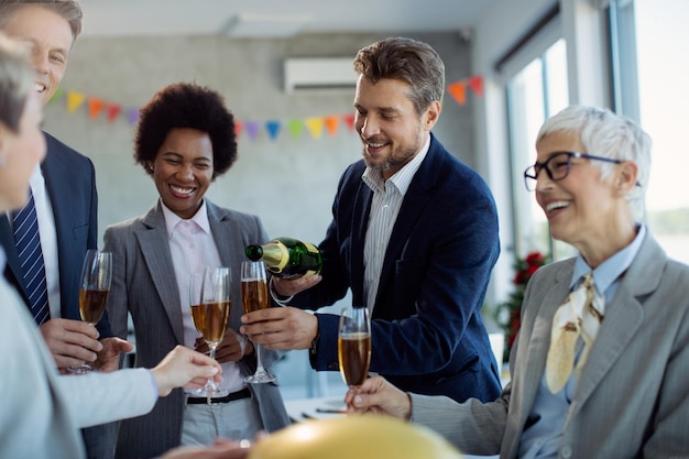 Heureux homme d'affaires versant du champagne à ses collègues tout en célébrant au bureau