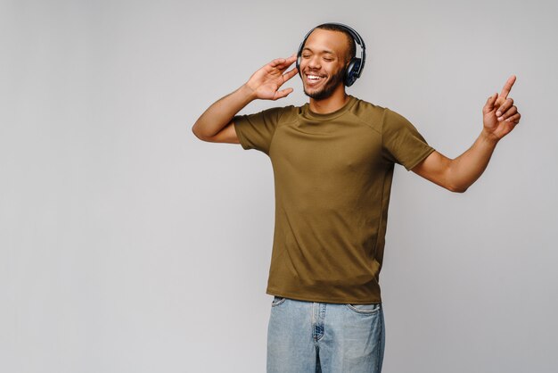 Heureux homme africain souriant à l'écoute de la musique dans les écouteurs sur mur gris