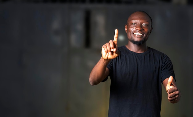 Heureux homme africain sur un t-shirt noir levant les pouces tout en appuyant sur un écran transparent