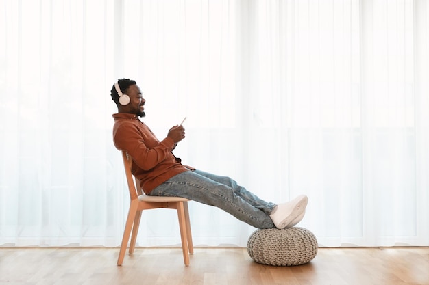 Heureux homme afro-américain écoutant de la musique sur un téléphone portable à la maison