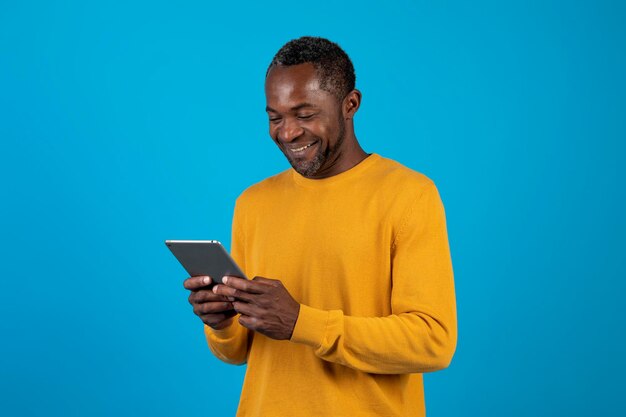 Heureux homme afro-américain utilisant une tablette numérique isolée sur bleu