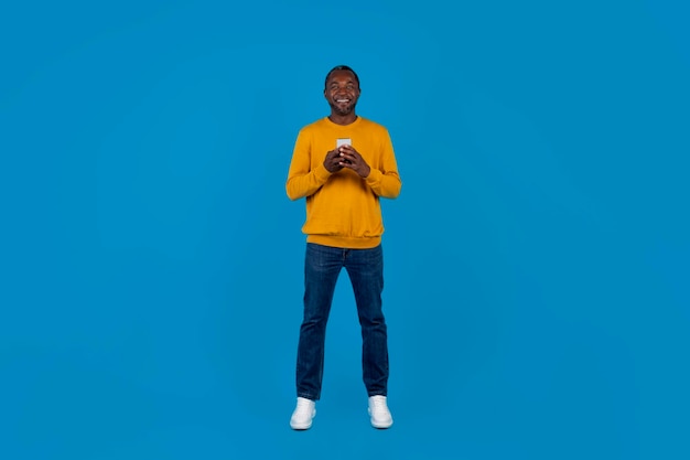 Heureux homme afro-américain utilisant un téléphone portable sur bleu