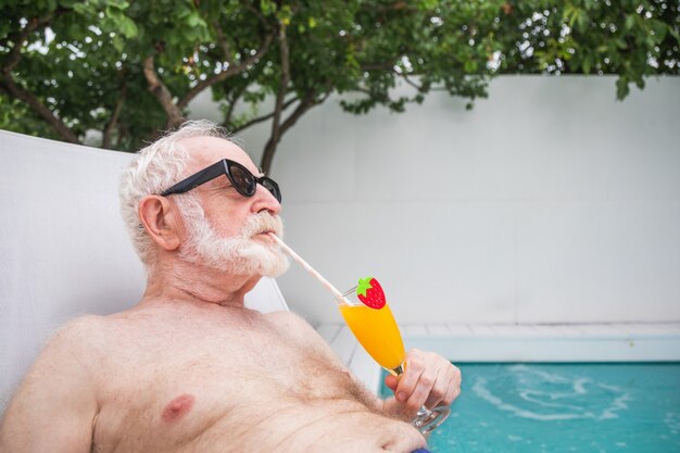 Heureux homme âgé faisant la fête dans la piscine - Personne âgée active prenant un bain de soleil et se relaxant dans une piscine privée pendant l'été