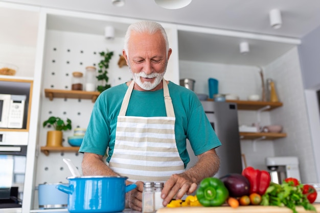 Heureux homme âgé s'amusant à cuisiner à la maison Personne âgée préparant un déjeuner santé dans une cuisine moderne Temps de vie à la retraite et concept de nutrition alimentaire