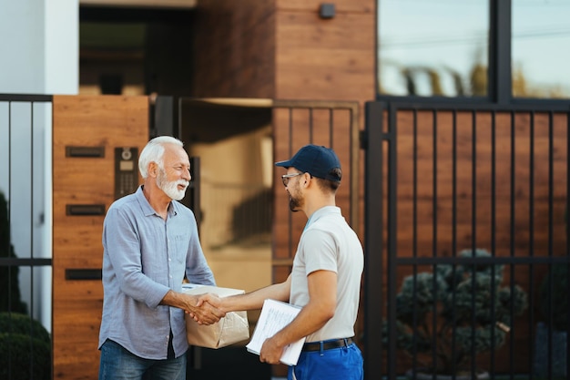 Heureux homme âgé serrant la main d'un courrier tout en faisant livrer son colis