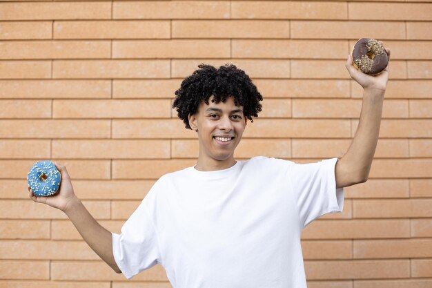 Heureux homme américain souriant vêtu d'un t-shirt blanc tenant du chocolat et des beignets bleus sur les côtés