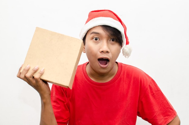 heureux homme asiatique attrayant dans le thème de Noël rouge tenant une boîte en papier de cadeau. annonces de Noël.