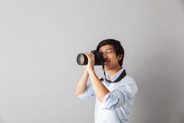 Heureux homme asiatique debout isolé, prenant une photo avec appareil photo