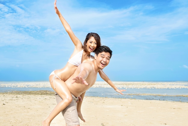 Heureux homme asiatique portant une fille sur le dos sur la plage