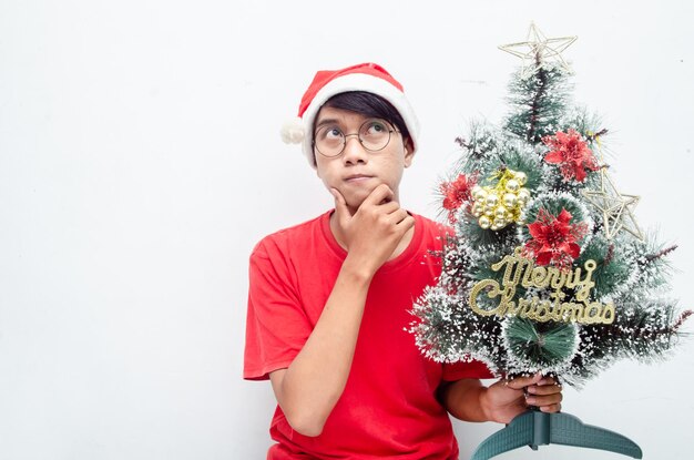 Heureux homme asiatique séduisant en vêtements rouges sur le thème de Noël tout en tenant un sapin de Noël