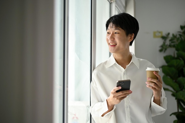 Heureux homme asiatique avec son smartphone et sa tasse de café rêvant de sa carrière