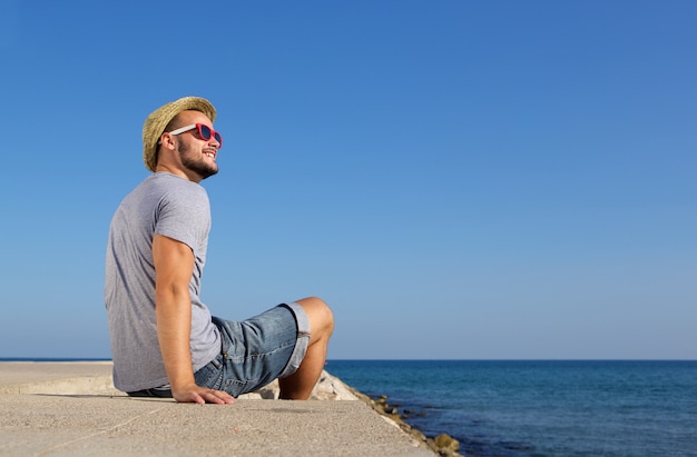 Heureux homme assis au bord de la mer avec un chapeau