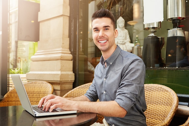 Heureux homme assis au café travaillant sur un ordinateur portable à l&#39;extérieur