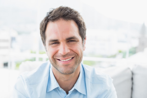 Heureux homme assis sur le canapé en souriant à la caméra