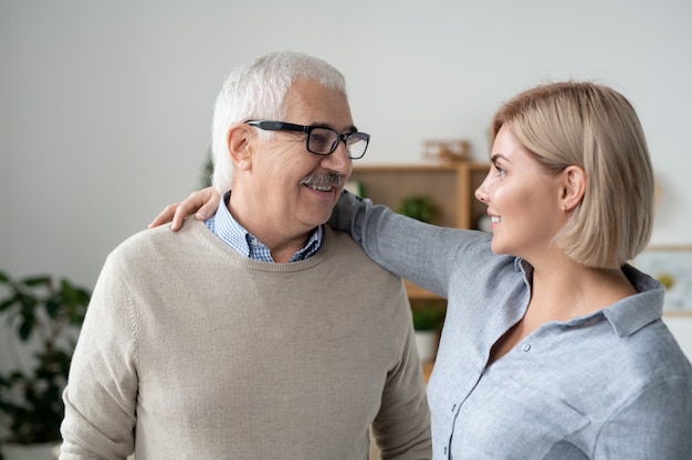 Heureux homme aux cheveux gris mature dans des lunettes et des vêtements décontractés et sa jeune fille blonde embrassant et se regardant