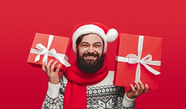 Heureux homme barbu en bonnet de Noel souriant et montrant des cadeaux emballés