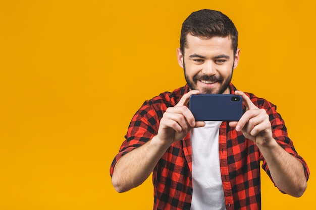 Heureux homme barbu en chemise à carreaux jouant sur smartphone isolé sur mur jaune.