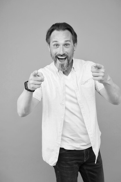 Heureux homme barbu avec des cheveux de barbe élégants dans un style de mode décontracté pointant l'index publicité sur fond gris