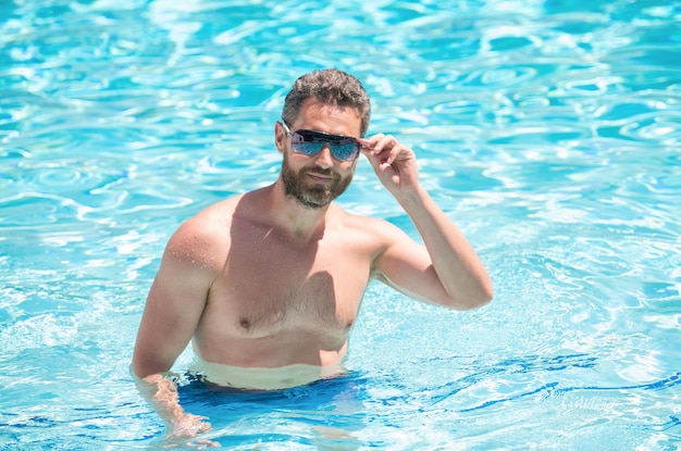 Heureux homme barbu à lunettes nageant dans la piscine en été se détendre