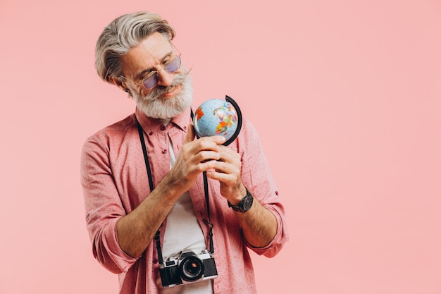 Heureux l'homme barbu à lunettes de soleil avec un appareil photo choisit un pays sur le globe pour voyager.