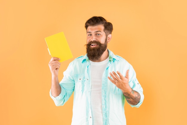 Heureux homme barbu présentant un livre sur une publicité de fond jaune