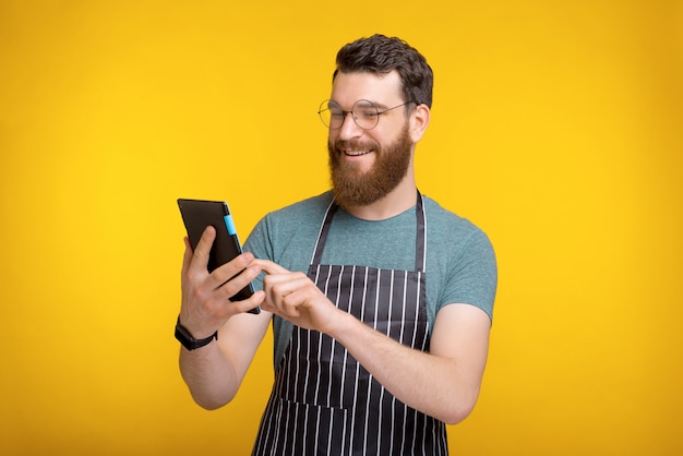 Heureux homme barbu en uniforme et à l'aide de tablette sur jaune