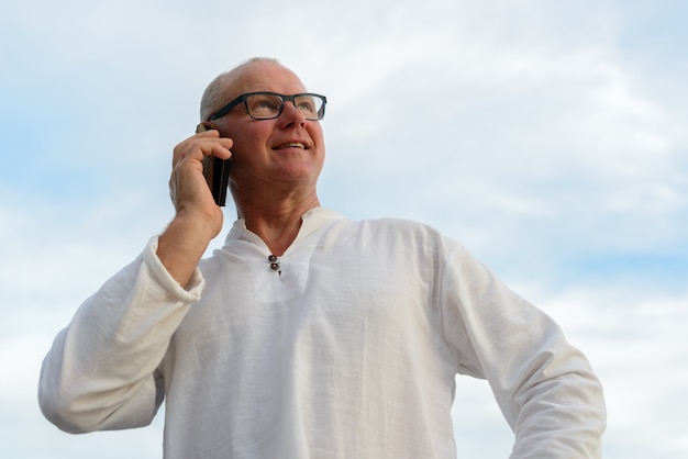 Heureux homme beau touriste mature parlant au téléphone contre vue sur la plage en plein air