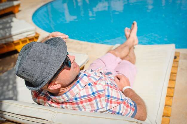 Heureux homme avec un chapeau allongé sur un transat au bord de la piscine