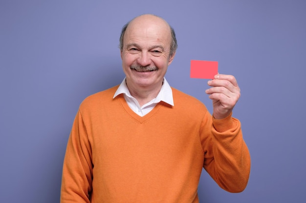 Heureux homme chauve hispanique senior publicité carte bonus souriant à la caméra