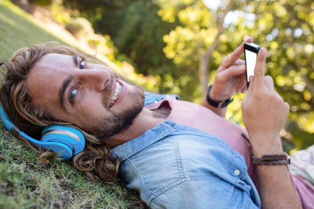 Heureux homme couché sur l'herbe, écouter de la musique sur téléphone mobile