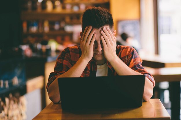 Heureux homme décontracté à l'aide de smartphone et ordinateur portable dans un café sous le stress et la préparation aux examens