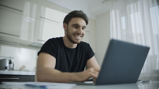 Heureux homme discutant en ligne sur un ordinateur portable à la maison