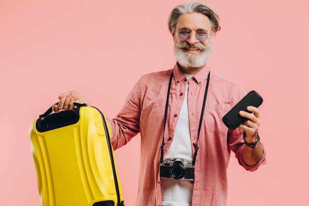 Heureux homme élégant barbu en lunettes de soleil avec appareil photo tenant une valise et un haut-parleur portable