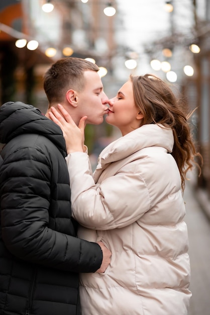 Heureux homme embrassant sa femme dans la rue. Le mec amoureux s'occupe de la fille. Couple profitant de la vie à l'extérieur. Le concept de lumière saint valentin, cadeaux